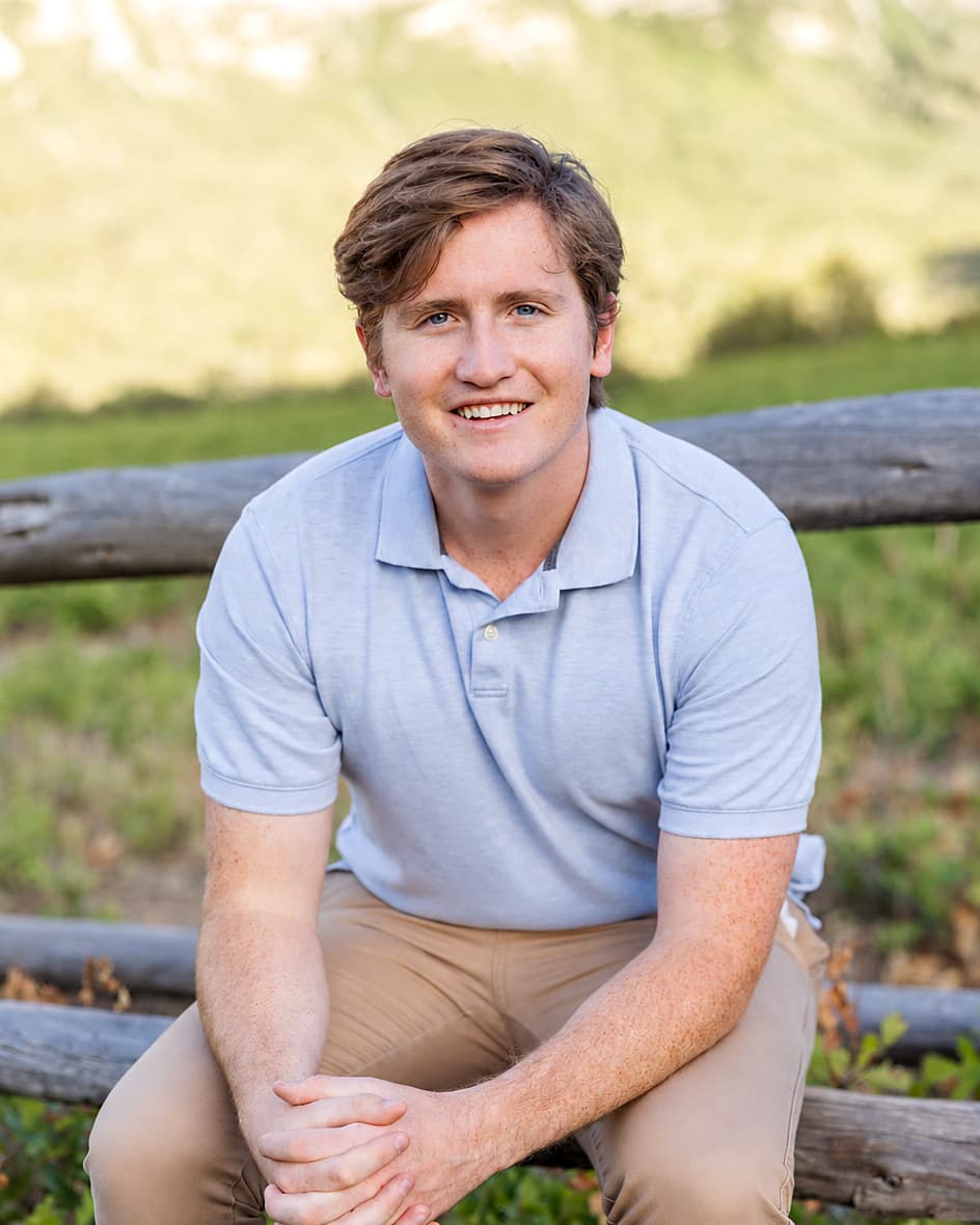 Ewan Morkel, Enrolled Agent and founder of Morkel Financial, seated on a fence rail below the Wasatch foothills in Mapleton, Utah